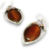 A pair of silver wire-wrapped drop earrings featuring large, polished brown tiger's eye stones, accented with small beads and a clear crystal on a white background.