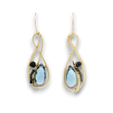 A pair of gold dangle earrings featuring teardrop-shaped light blue gemstones, small black round beads, and a tiny dark stone accent, shown on a plain white background.