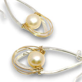 A pair of teardrop-shaped earrings featuring a round cream pearl wrapped in twisted gold and silver wire, set against a plain white background.