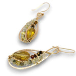 A pair of gold drop earrings featuring a large teardrop-shaped yellow gemstone, accented with small round beads in green, white, and brown, set in a textured gold frame on a white background.