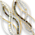 Close-up of a jewelry strand featuring layered organic wavy metal wires in gold and silver tones, interspersed with strands of faceted beads in smoky brown, translucent white, and amber.