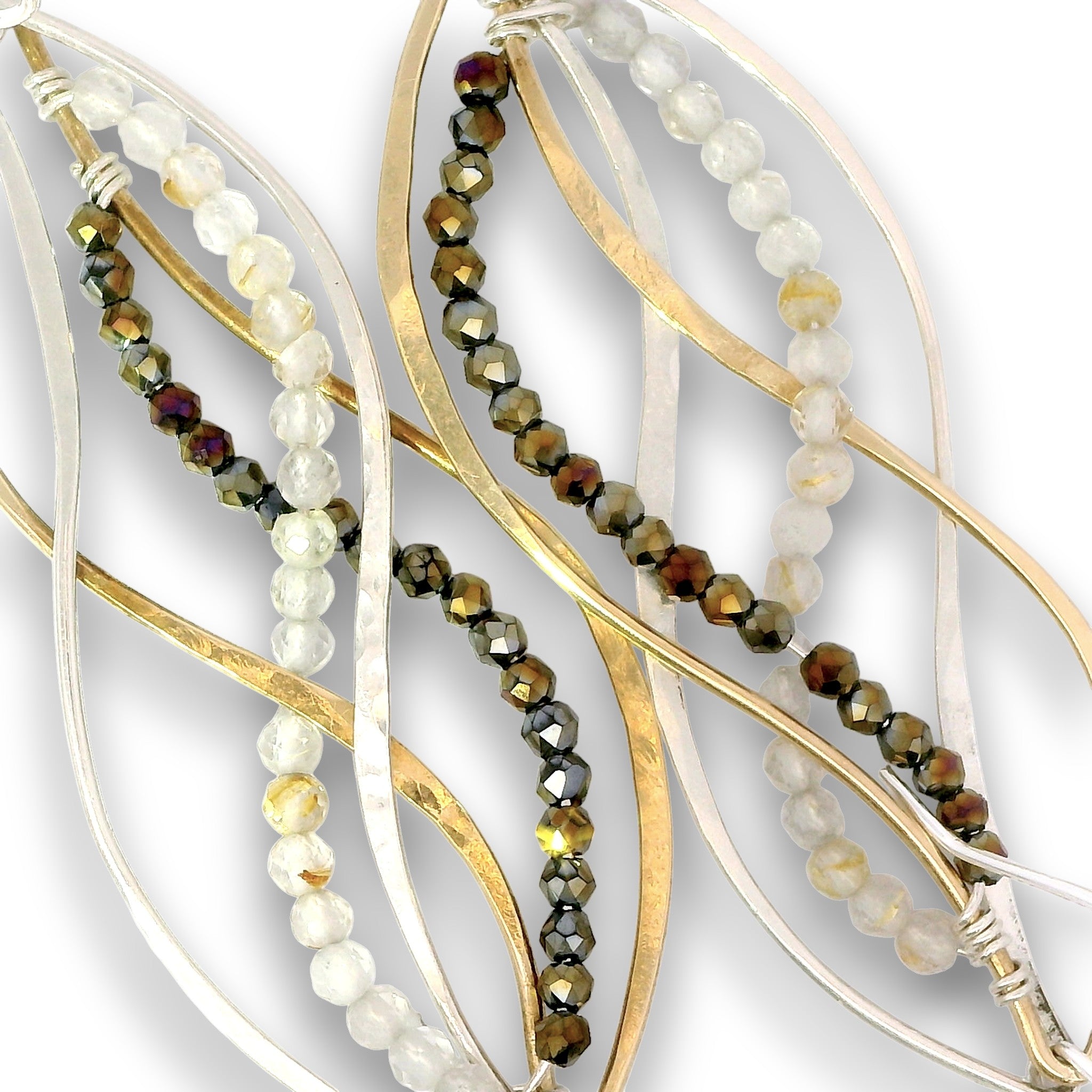 Close-up of a jewelry strand featuring layered organic wavy metal wires in gold and silver tones, interspersed with strands of faceted beads in smoky brown, translucent white, and amber.
