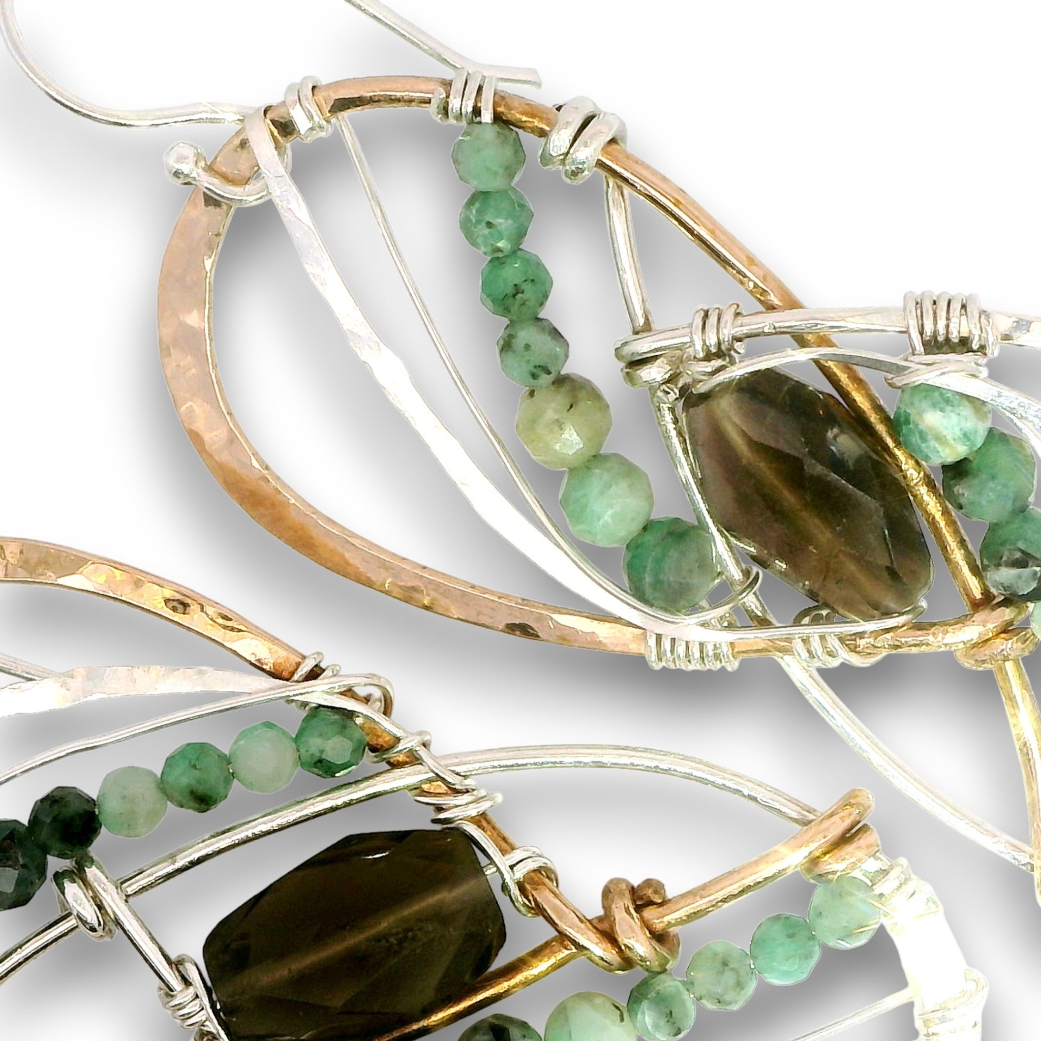 Close-up of handmade wire-wrapped earrings featuring green and smoky brown gemstone beads, with silver and gold-toned metal wires on a white background.