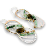 A pair of handmade dangle earrings featuring clear quartz crystal loops, green beads, a dark brown teardrop gemstone, and rose gold and silver wire wrapping on a white background.