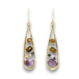 A pair of gold teardrop dangle earrings featuring various gemstones including a prominent purple amethyst, brown tiger's eye, and smaller pink and green stones, set against a plain white background.