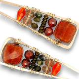 Two rectangular gold wire-wrapped jewelry pieces with large faceted orange-brown stones, smaller red beads, dark metallic beads, and translucent brown beads, shown on a white background.