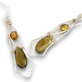 A pair of handmade dangle earrings featuring olive green teardrop-shaped smoky quartz stones, a smaller round brown tiger's eye bead, and silver wire frames with gold accents, shown on a white background.