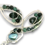 A pair of silver wire-wrapped earrings featuring faceted dark green tourmaline beads and a large iridescent green pearl, set against a plain white background.