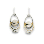 A pair of teardrop-shaped dangle earrings featuring a central round white stone with dark inclusions, surrounded by layered silver and gold-tone metal rings and small clear faceted beads, shown on a plain white background.