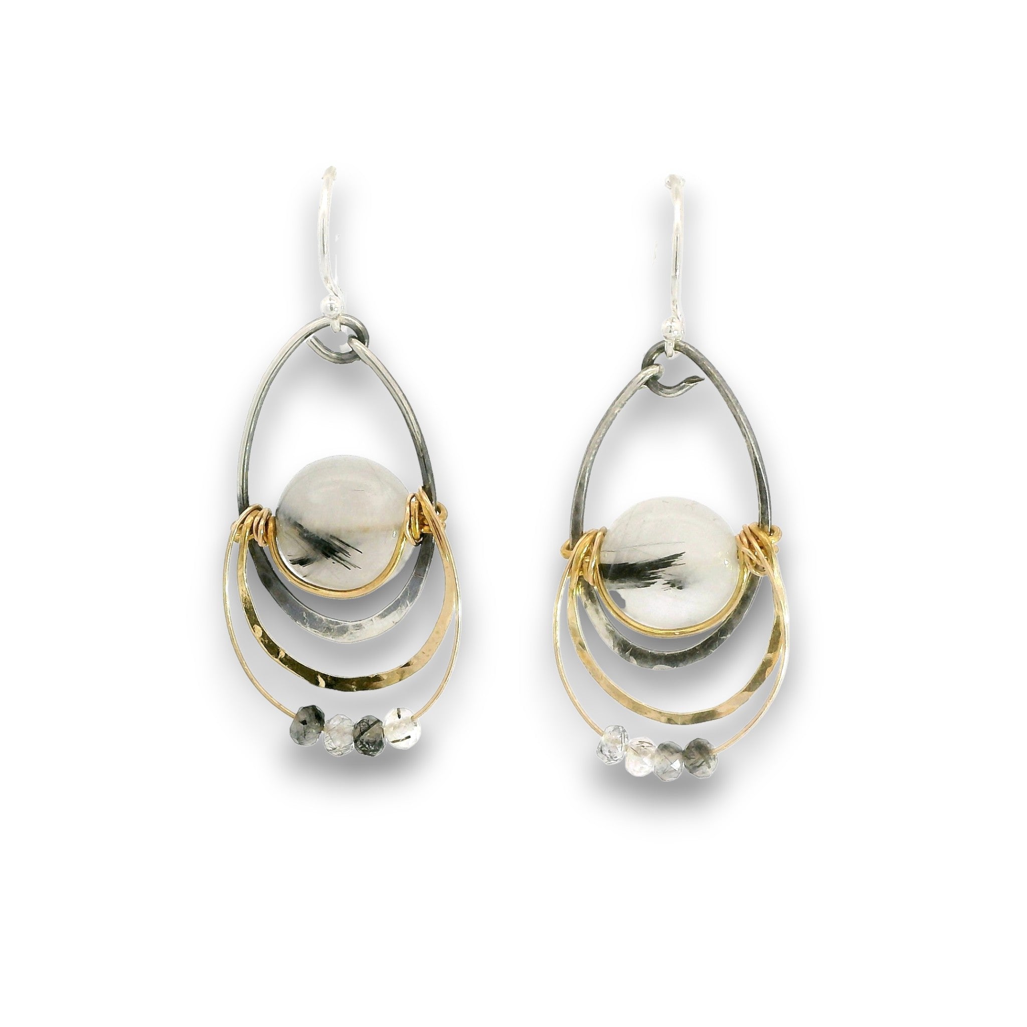 A pair of teardrop-shaped dangle earrings featuring a central round white stone with dark inclusions, surrounded by layered silver and gold-tone metal rings and small clear faceted beads, shown on a plain white background.
