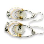 A pair of handmade teardrop dangle earrings featuring a central round white stone with black inclusions, surrounded by layered silver and gold wire loops, small clear beads, and silver fishhook wires, shown on a white background.