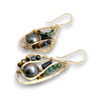 A pair of gold teardrop dangle earrings featuring a large dark gray freshwater pearl, green and brown beads, and small black faceted stones, shown on a white background.