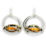 A pair of silver dangle earrings featuring a double-ring circular design with a central horizontal oval containing amber-colored resin and small green and brown beads, shown on a white background.