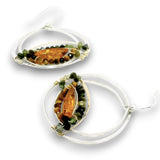 A pair of silver hoop earrings with oval bezel settings holding a polished amber-orange center stone, surrounded by rows of small green and brown beads, on a white background.