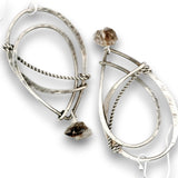 A pair of silver-toned geometric dangle earrings with hammered and twisted wire details, each featuring a small rough brown stone at the top and a larger polished stone at the bottom, shown on a white background.