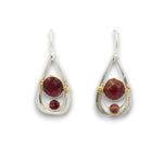 A pair of teardrop-shaped dangle earrings featuring round and round-cut deep red gemstones in silver and gold wire-wrapped settings, shown against a plain white background.