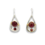 A pair of teardrop-shaped dangle earrings featuring round and round-cut deep red gemstones in silver and gold wire-wrapped settings, shown against a plain white background.