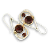 A pair of teardrop-shaped dangle earrings featuring large oval dark red garnet stones and smaller round garnet beads, set in silver and gold-tone metal with textured silver borders, on a white background.