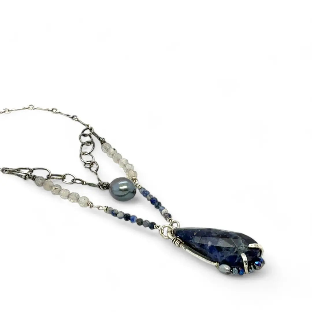 A sterling silver necklace with a handmade prong pendant featuring a deep blue sodalite natural gemstone, micro faceted sodalite and labradorite gemstones, and a lustrous gray blue fresh water pearl, connected to an oxidized link chain.