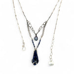 A sterling silver necklace with a handmade prong pendant featuring a deep blue sodalite natural gemstone, micro faceted sodalite and labradorite gemstones, and a lustrous gray blue fresh water pearl, connected to an oxidized link chain.