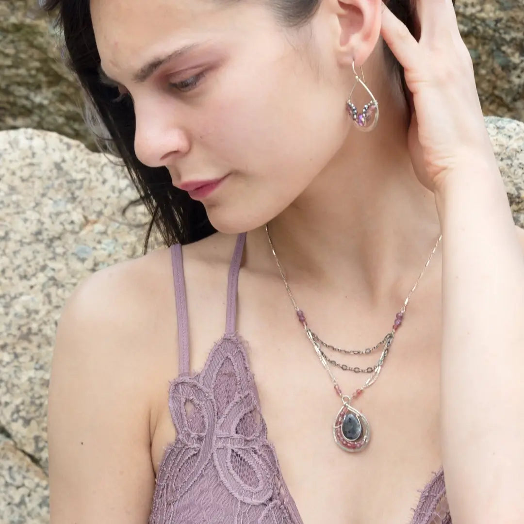 Larvikite and pink tourmaline gemstones are held within a sterling silver floral stamped drop pendant held on a layered chain made up of oxidized sterling silver textured and bright sterling tube chains necklace