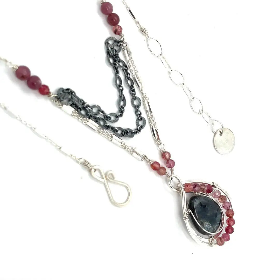 Larvikite and pink tourmaline gemstones are held within a sterling silver floral stamped drop pendant held on a layered chain made up of oxidized sterling silver textured and bright sterling tube chains necklace