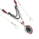 Larvikite and pink tourmaline gemstones are held within a sterling silver floral stamped drop pendant held on a layered chain made up of oxidized sterling silver textured and bright sterling tube chains necklace