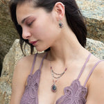 Larvikite and pink tourmaline gemstones are held within a sterling silver floral stamped drop pendant held on a layered chain made up of oxidized sterling silver textured and bright sterling tube chains necklace