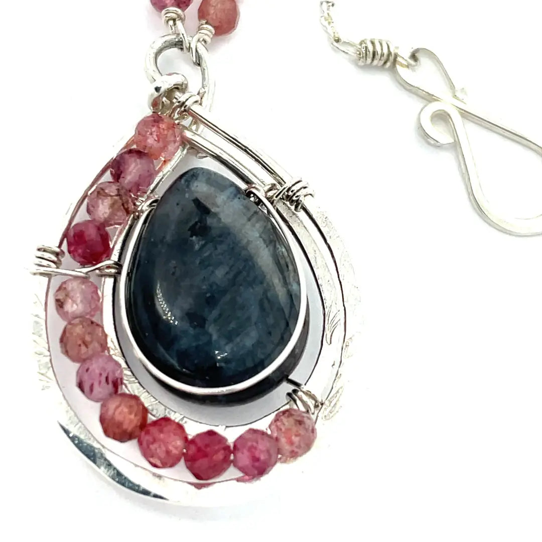 Larvikite and pink tourmaline gemstones are held within a sterling silver floral stamped drop pendant held on a layered chain made up of oxidized sterling silver textured and bright sterling tube chains necklace