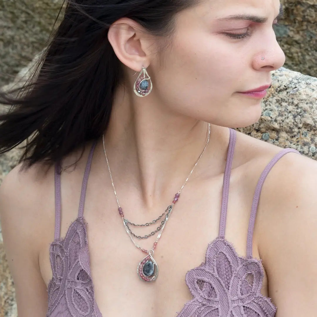 Larvikite and pink tourmaline gemstones are held within a sterling silver floral stamped drop pendant held on a layered chain made up of oxidized sterling silver textured and bright sterling tube chains necklace