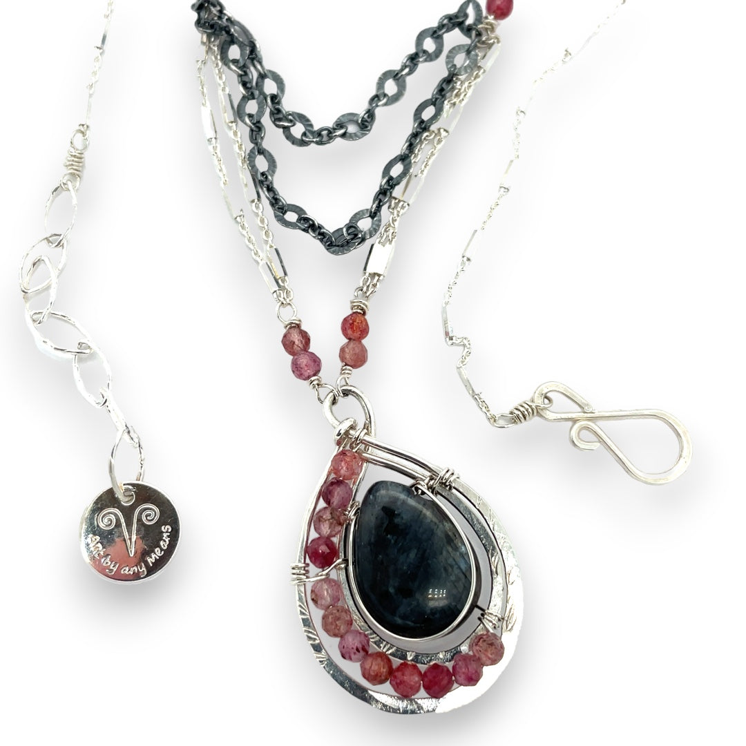 Larvikite and pink tourmaline gemstones are held within a sterling silver floral stamped drop pendant held on a layered chain made up of oxidized sterling silver textured and bright sterling tube chains necklace