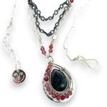 Larvikite and pink tourmaline gemstones are held within a sterling silver floral stamped drop pendant held on a layered chain made up of oxidized sterling silver textured and bright sterling tube chains necklace
