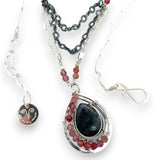 Larvikite and pink tourmaline gemstones are held within a sterling silver floral stamped drop pendant held on a layered chain made up of oxidized sterling silver textured and bright sterling tube chains necklace