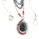 Larvikite and pink tourmaline gemstones are held within a sterling silver floral stamped drop pendant held on a layered chain made up of oxidized sterling silver textured and bright sterling tube chains necklace