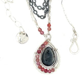 Larvikite and pink tourmaline gemstones are held within a sterling silver floral stamped drop pendant held on a layered chain made up of oxidized sterling silver textured and bright sterling tube chains necklace