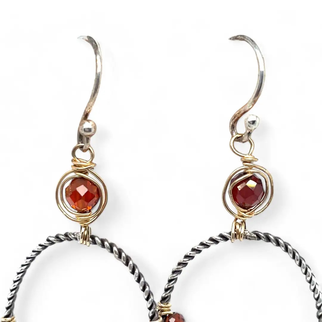 A pair of twisted oxidized sterling silver hoop earrings with garnet gemstone accents and faceted hessonite garnets on gold filled wire