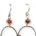 A pair of twisted oxidized sterling silver hoop earrings with garnet gemstone accents and faceted hessonite garnets on gold filled wire
