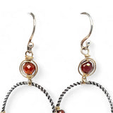 A pair of twisted oxidized sterling silver hoop earrings with garnet gemstone accents and faceted hessonite garnets on gold filled wire