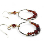 A pair of twisted oxidized sterling silver hoop earrings with garnet gemstone accents and faceted hessonite garnets on gold filled wire
