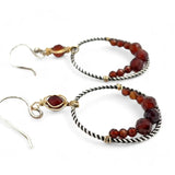 A pair of twisted oxidized sterling silver hoop earrings with garnet gemstone accents and faceted hessonite garnets on gold filled wire
