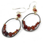 A pair of twisted oxidized sterling silver hoop earrings with garnet gemstone accents and faceted hessonite garnets on gold filled wire