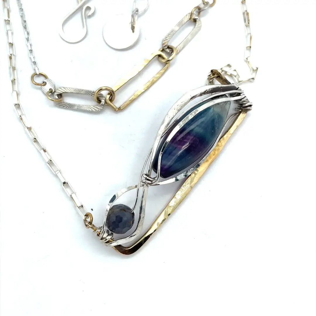 A double strand necklace with a geometric design, featuring fluorite and iolite faceted gemstones, hammered sterling silver, textured sterling silver links and handmade brass rings