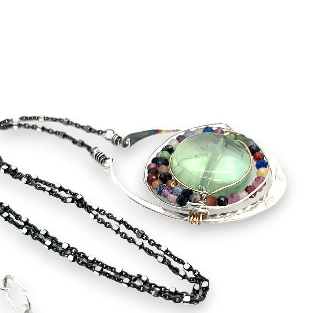 A sterling silver oval pendant necklace with a green fluorite smooth coin and micro faceted mixed gemstones, featuring an oxidized sterling silver dot chain 
