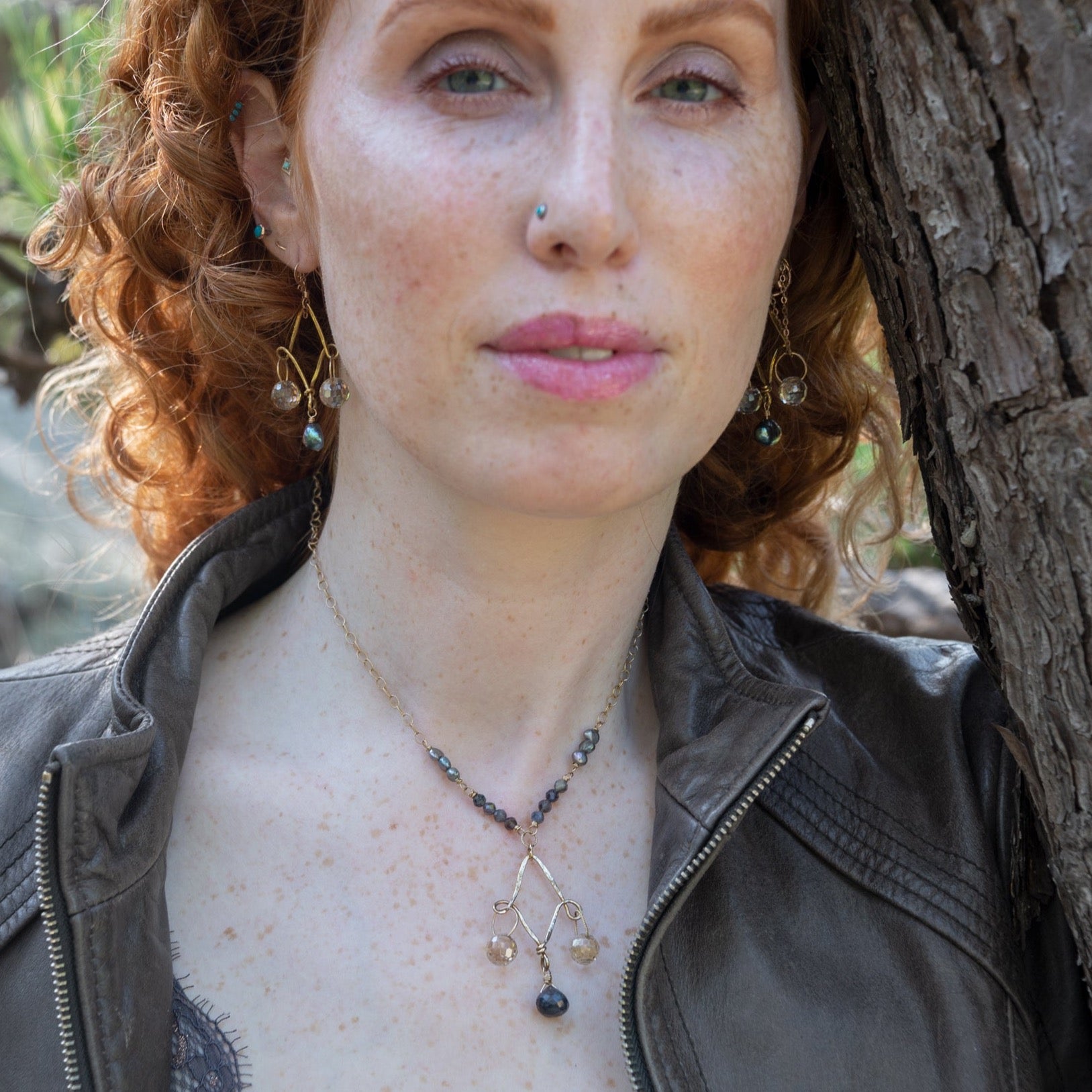 A woman wearing a brass chandelier necklace with a blue labradorite drop, gold-filled textured chain, with pearl and iolite gemstone embellishments.