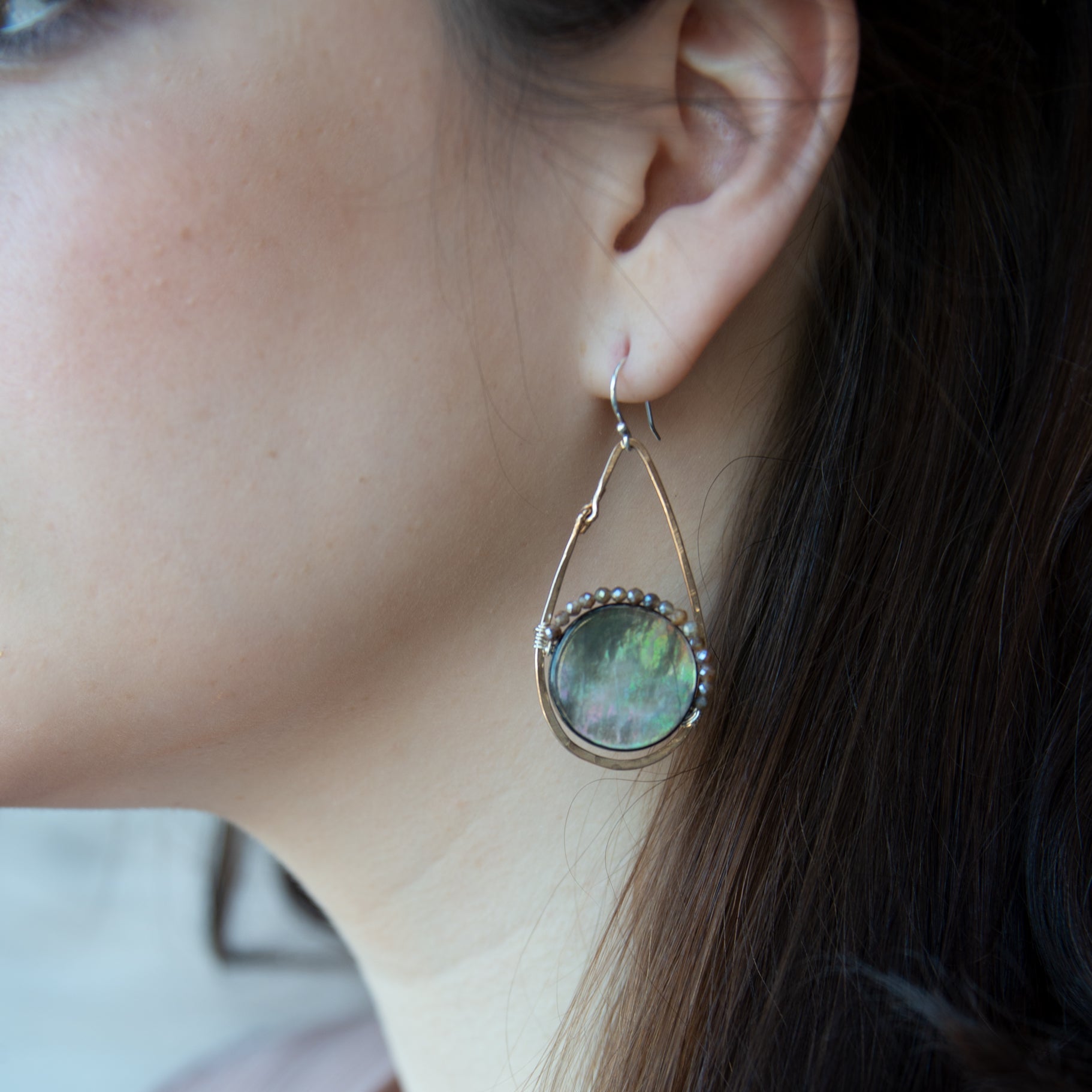 Iridescent abalone shell coins are surrounded by mauve moonstone gems within bronze teardrop earrings
