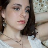 Iridescent abalone shell coins are surrounded by mauve moonstone gems within bronze teardrop earrings