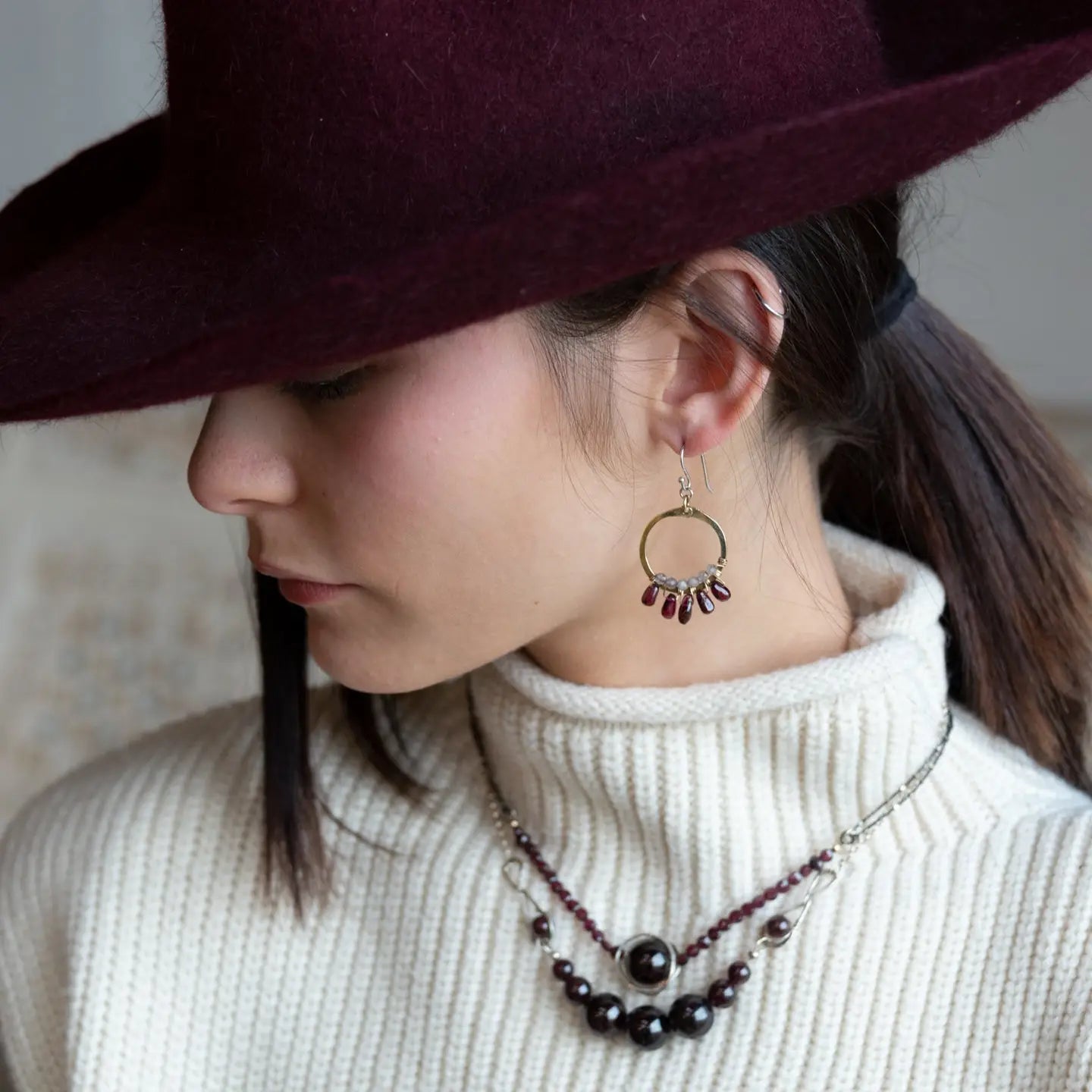 Smooth garnet drops line the bottom of a brass hammered hoop earring with the inside lined in faceted labradorite gemstones