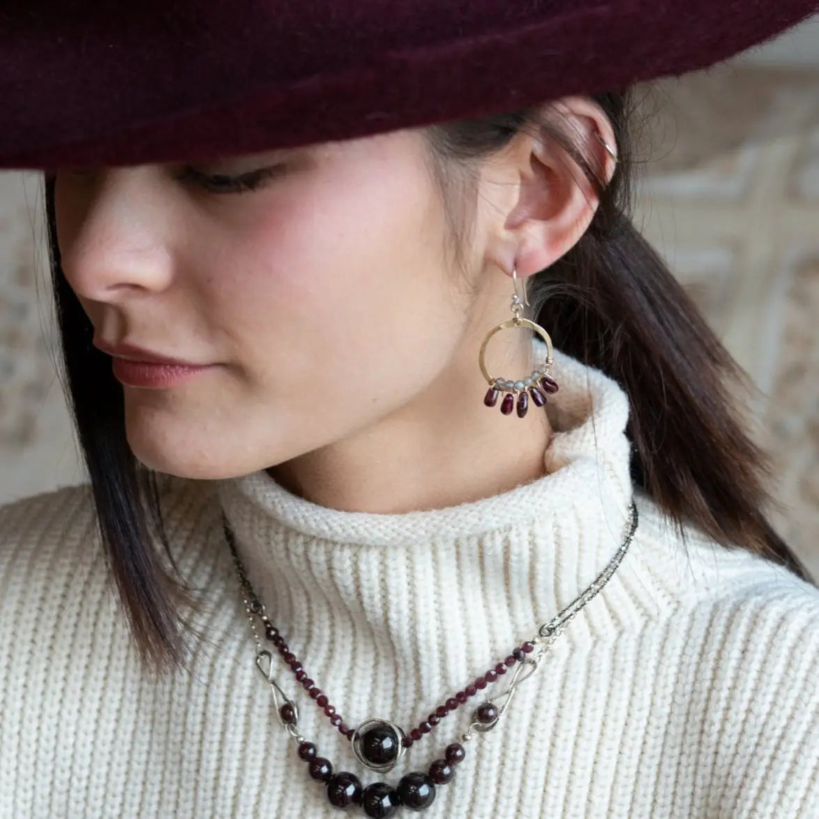Smooth garnet drops line the bottom of a brass hammered hoop earring with the inside lined in faceted labradorite gemstones