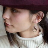 A pair of handmade petite double hoop earrings with red tiger's eye and garnet gemstones, set in hammered brass arches with sterling silver French hooks.