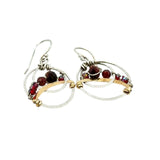A pair of handmade petite double hoop earrings with red tiger's eye and garnet gemstones, set in hammered brass arches with sterling silver French hooks.